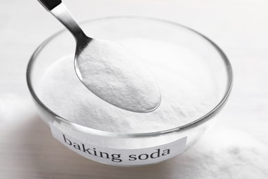 Photo of Taking baking soda from bowl at white wooden table, closeup
