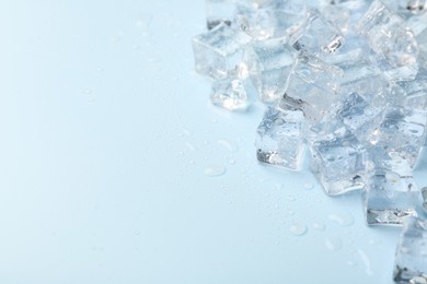Photo of Crystal clear ice cubes on light blue background, closeup. Space for text