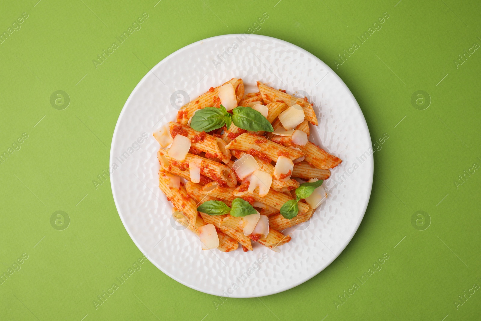 Photo of Tasty pasta with tomato sauce, cheese and basil on green background, top view