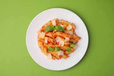 Tasty pasta with tomato sauce, cheese and basil on green background, top view