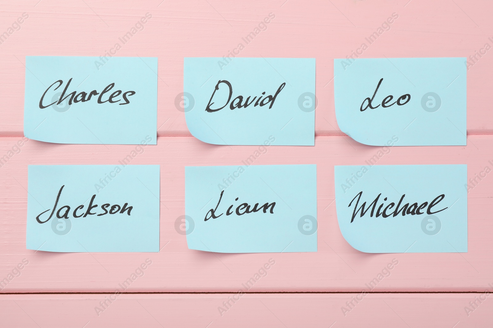 Photo of Paper stickers with different names on pink wooden background, flat lay. Choosing baby's name