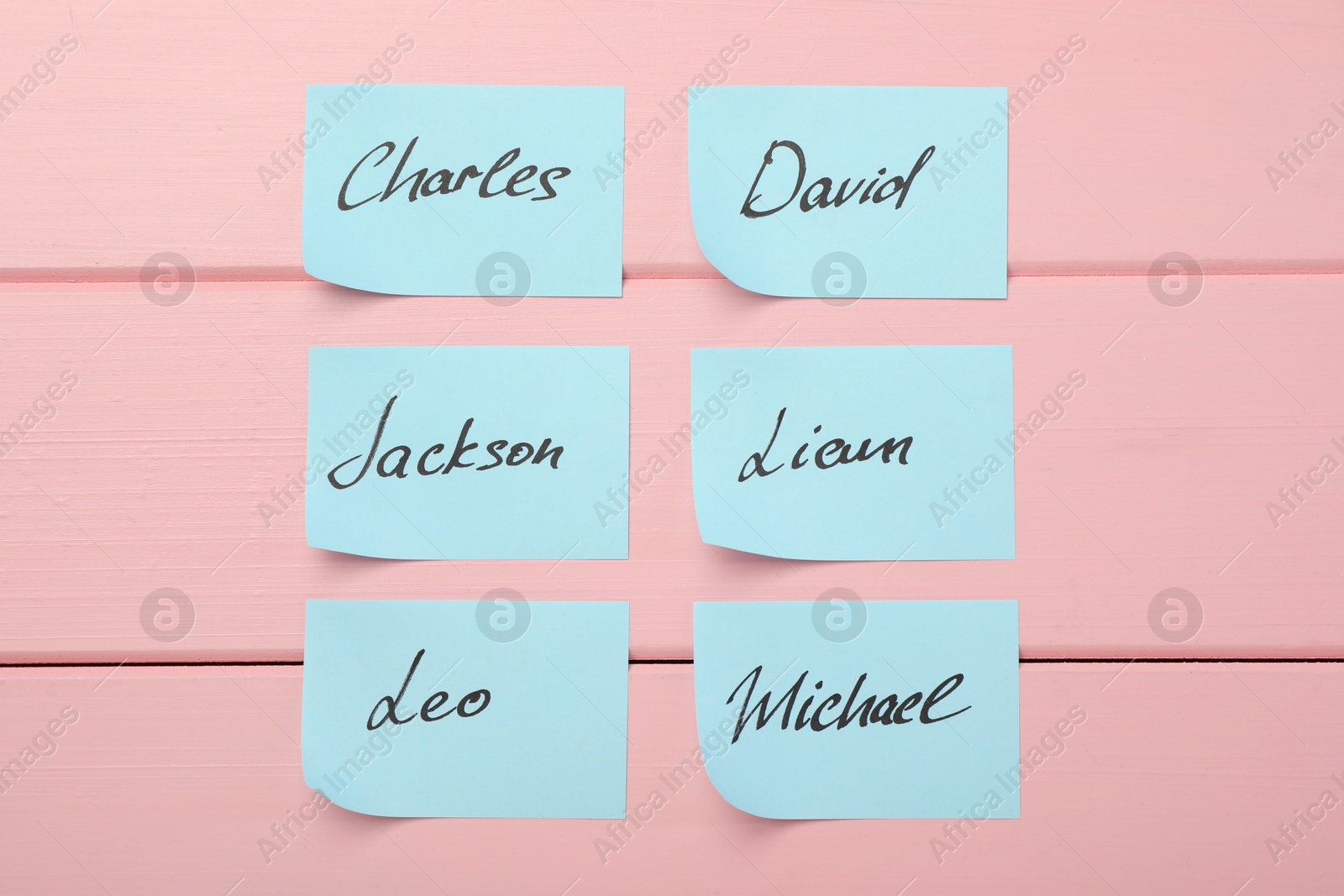 Photo of Paper stickers with different names on pink wooden background, flat lay. Choosing baby's name