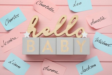 Cubes with phrase Hello Baby and paper stickers with different names on pink wooden background, flat lay. Choosing baby's name