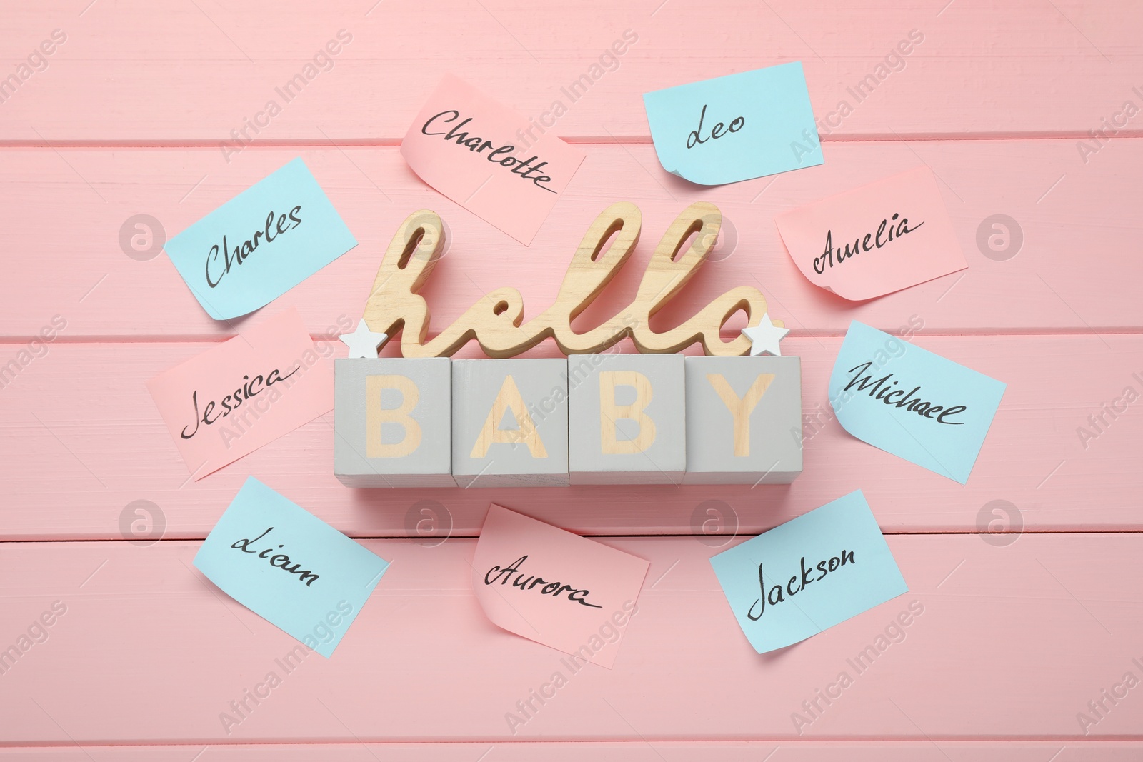 Photo of Cubes with phrase Hello Baby and paper stickers with different names on pink wooden background, flat lay. Choosing baby's name