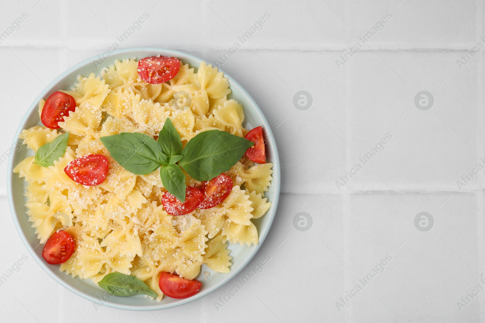 Photo of Tasty pasta with tomato, cheese and basil on white tiled table, top view. Space for text