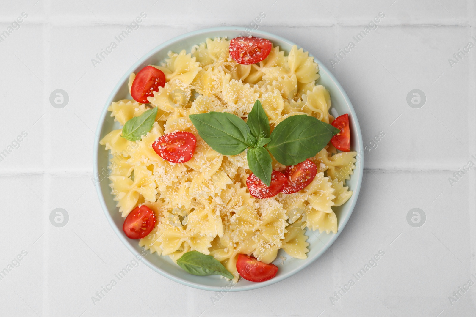 Photo of Tasty pasta with tomato, cheese and basil on white tiled table, top view