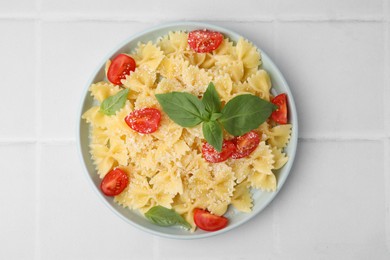 Photo of Tasty pasta with tomato, cheese and basil on white tiled table, top view