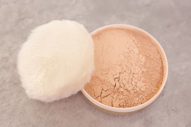 Face powder with puff applicator on grey textured table, above view