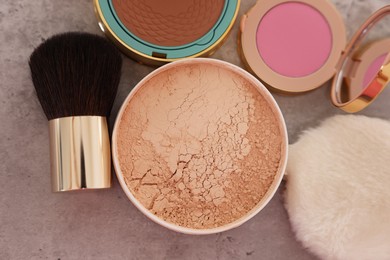 Photo of Bronzer, powder, blusher and brush on grey textured table, flat lay