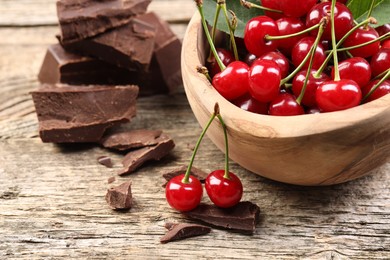 Photo of Fresh cherries in bowl and dark chocolate on wooden table, closeup