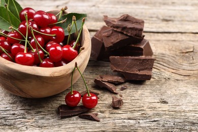 Photo of Fresh cherries in bowl and dark chocolate on wooden table