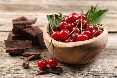 Fresh cherries in bowl and dark chocolate on wooden table, closeup