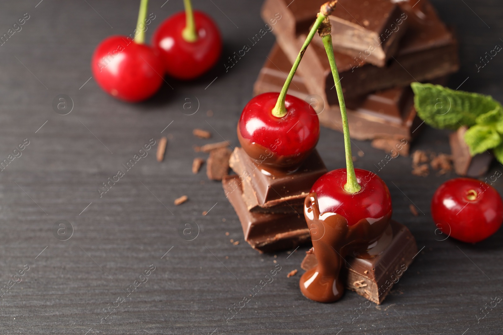 Photo of Fresh cherries with chocolate on grey wooden table, closeup. Space for text