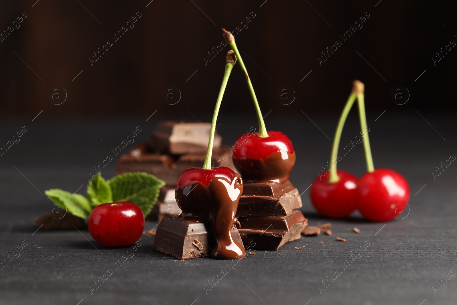 Photo of Fresh cherries with chocolate on grey wooden table, closeup