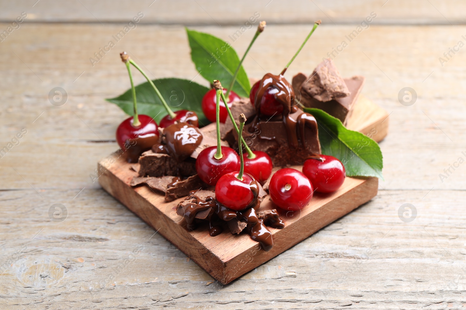 Photo of Fresh cherries with milk chocolate and green leaves on wooden table