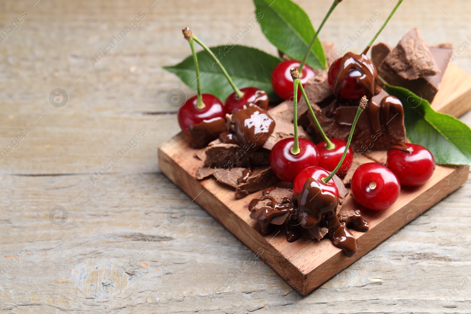 Photo of Fresh cherries with milk chocolate and green leaves on wooden table, space for text