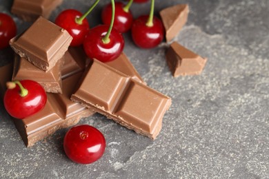 Fresh cherries with pieces of milk chocolate on grey textured table, space for text