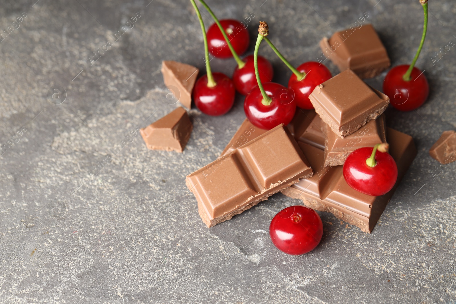 Photo of Fresh cherries with pieces of milk chocolate on grey textured table, space for text