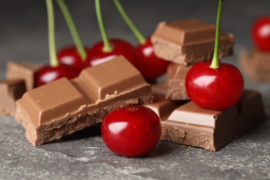 Fresh cherries with pieces of milk chocolate on grey textured table, closeup