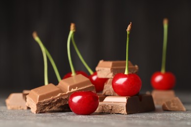 Fresh cherries with pieces of milk chocolate on grey textured table, closeup