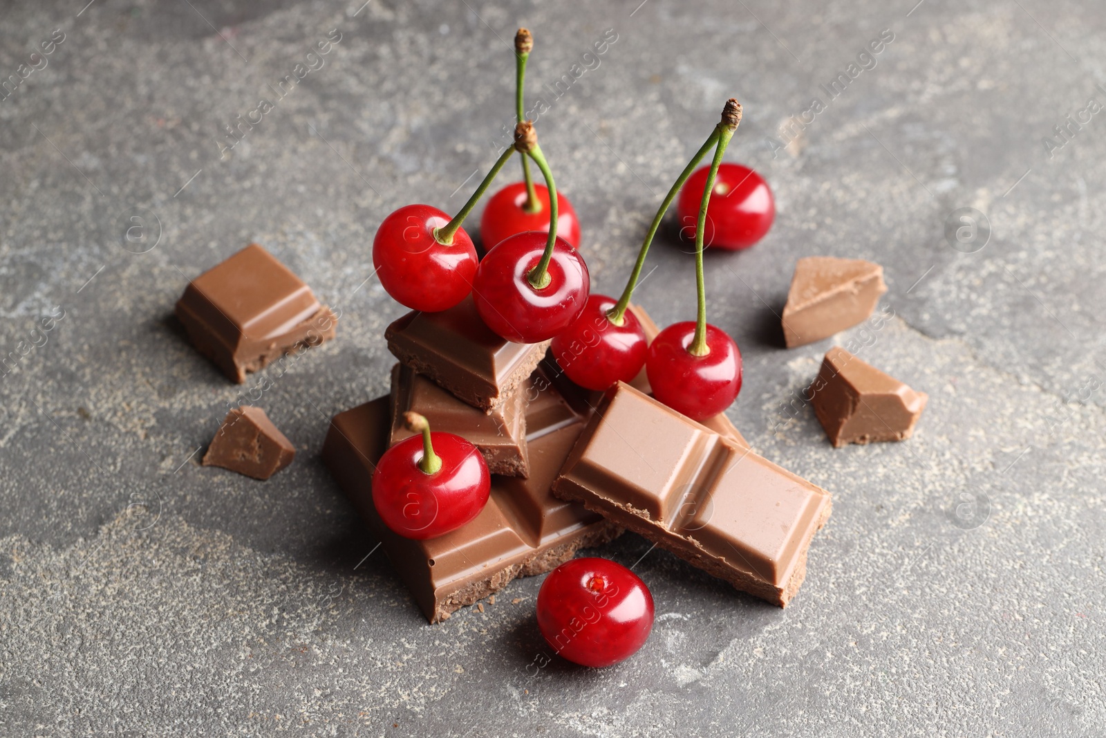 Photo of Fresh cherries with pieces of milk chocolate on grey textured table