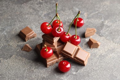 Photo of Fresh cherries with pieces of milk chocolate on grey textured table