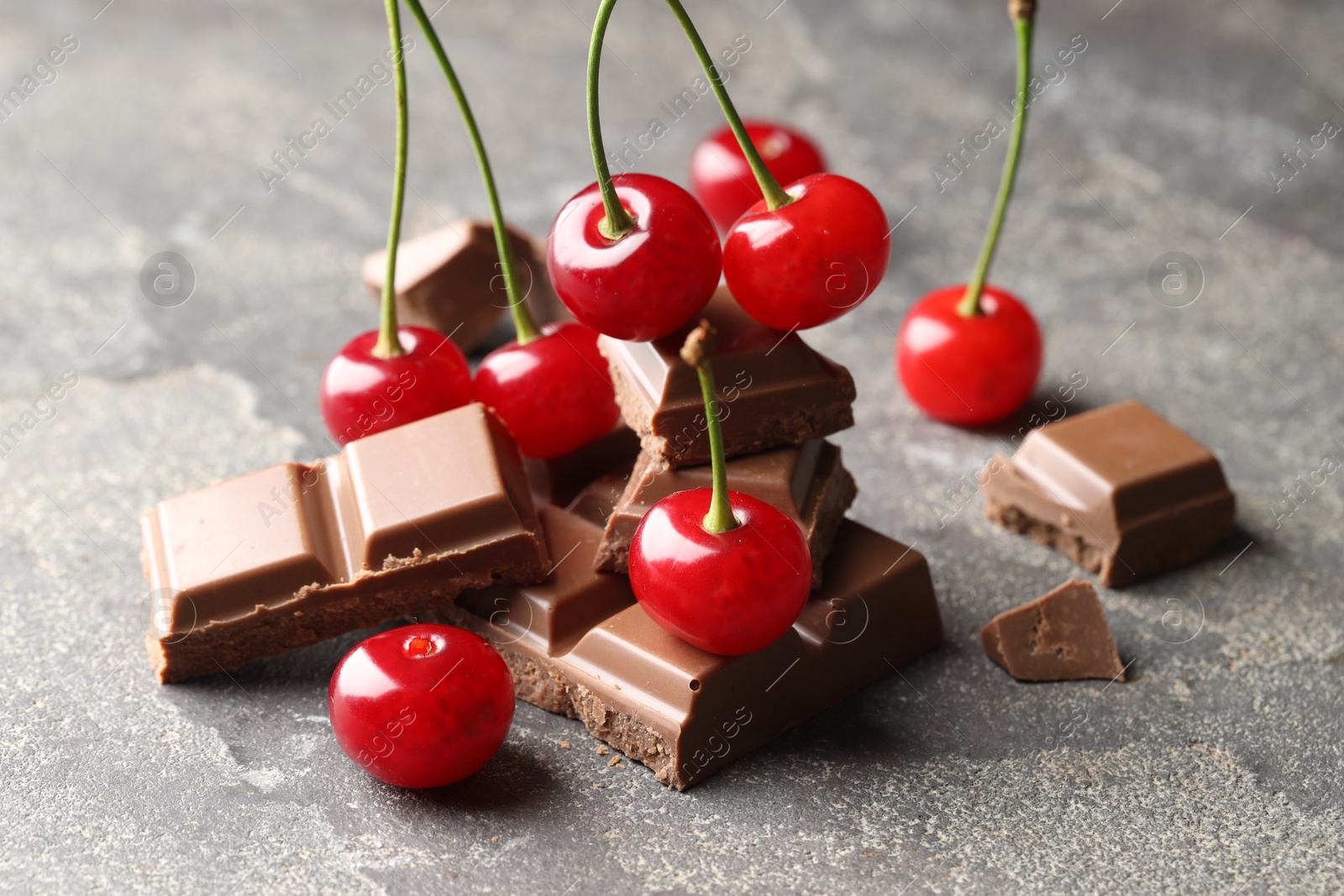 Photo of Fresh cherries with pieces of milk chocolate on grey textured table, closeup