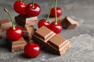 Photo of Fresh cherries with pieces of milk chocolate on grey textured table, closeup