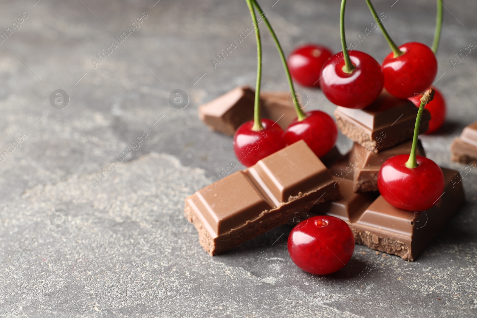 Photo of Fresh cherries with pieces of milk chocolate on grey textured table, closeup. Space for text