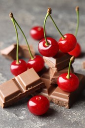 Photo of Fresh cherries with pieces of milk chocolate on grey textured table, closeup