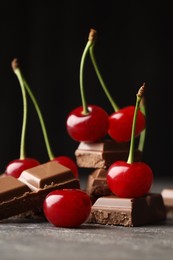 Photo of Fresh cherries with pieces of milk chocolate on grey textured table, closeup