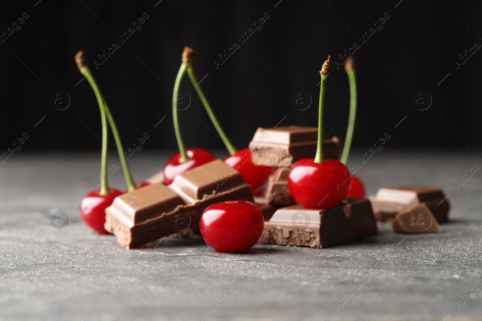 Photo of Fresh cherries with pieces of milk chocolate on grey textured table, closeup