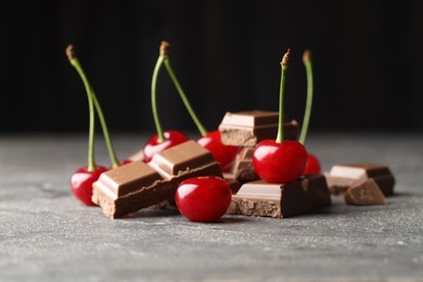 Photo of Fresh cherries with pieces of milk chocolate on grey textured table, closeup