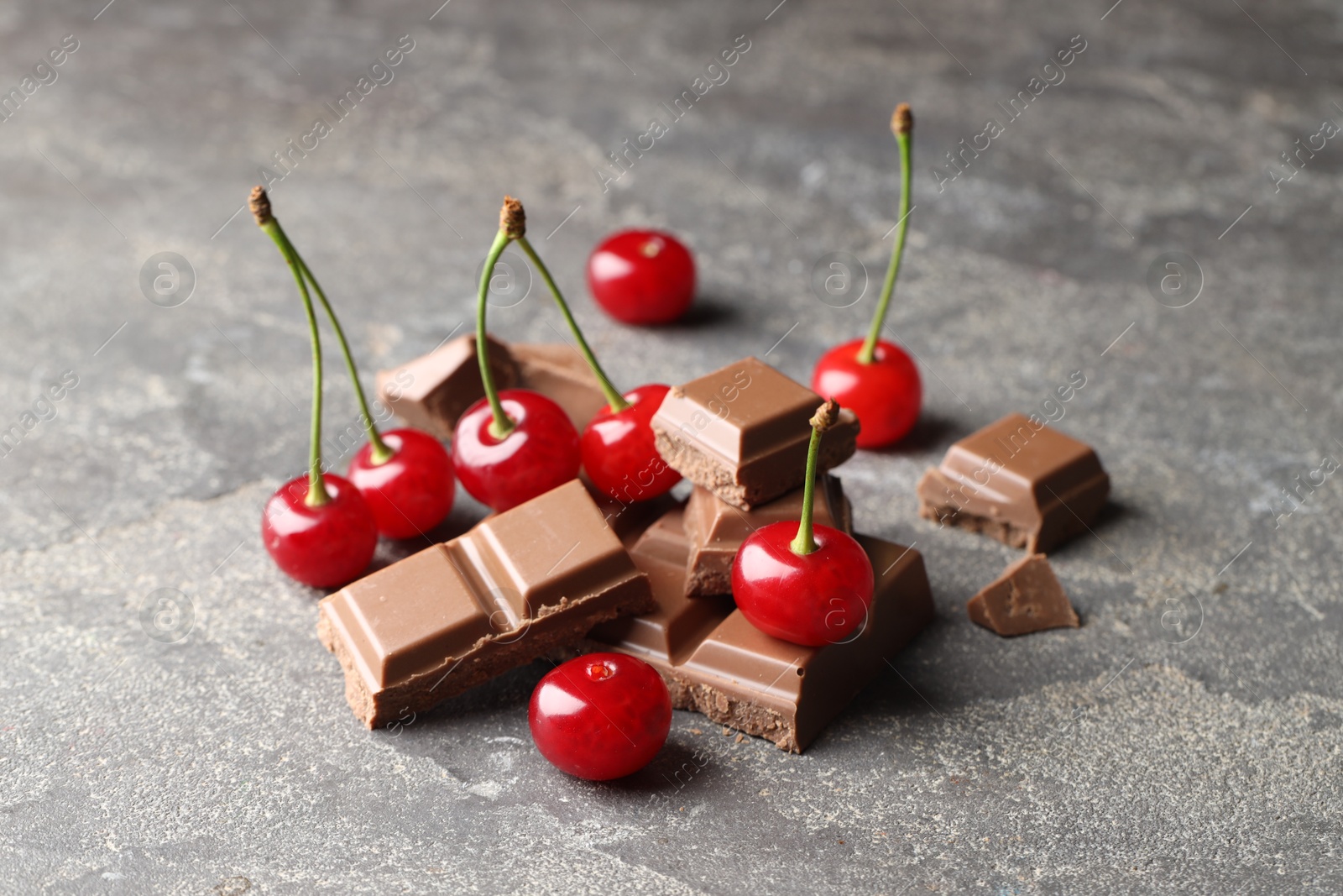 Photo of Fresh cherries with pieces of milk chocolate on grey textured table