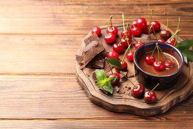 Photo of Fresh cherries with chocolate and mint on wooden table, space for text