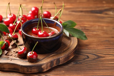 Fresh cherries with melted chocolate on wooden table, closeup. Space for text