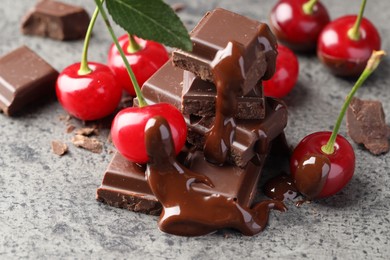 Photo of Fresh cherries with dark chocolate on grey textured table, closeup