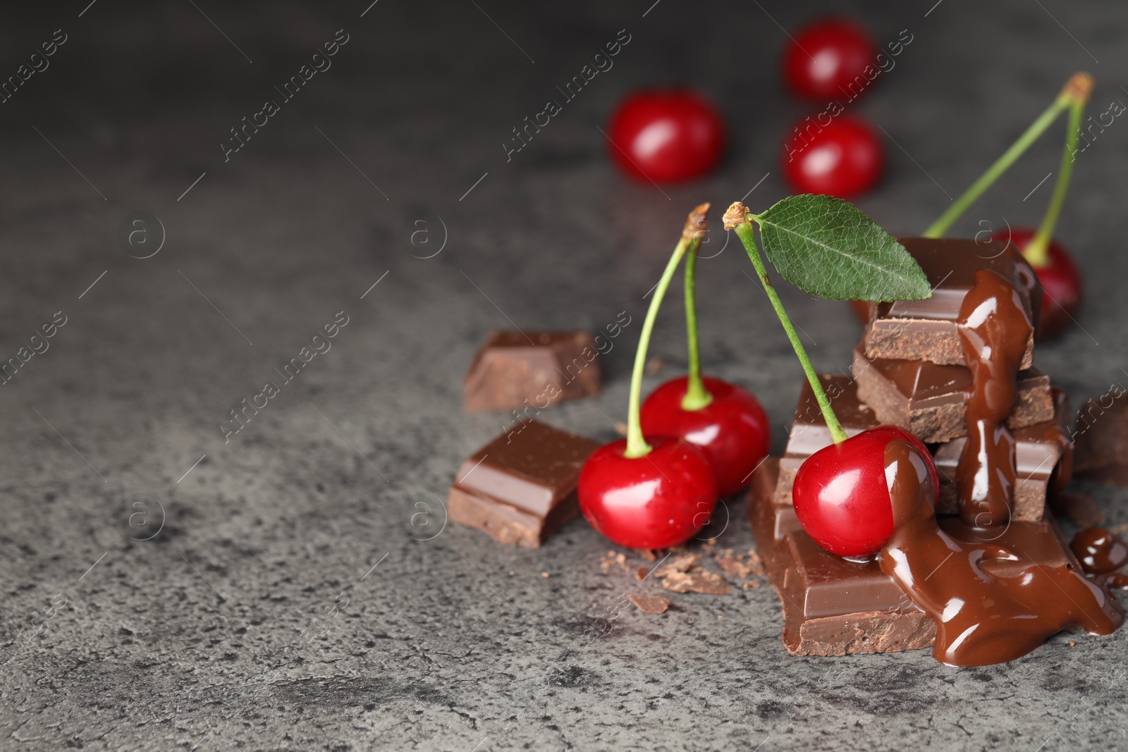 Photo of Fresh cherries with chocolate on grey textured table, space for text