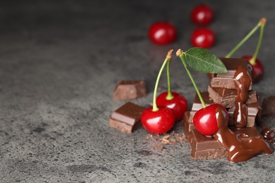 Photo of Fresh cherries with chocolate on grey textured table, space for text