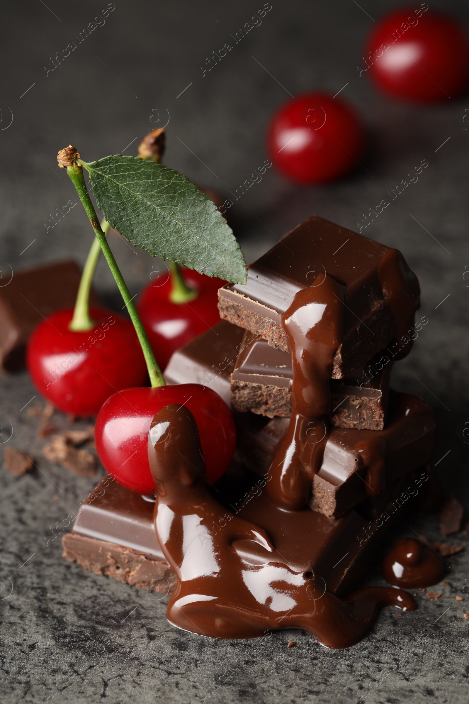 Photo of Fresh cherries with dark chocolate on grey textured table, closeup