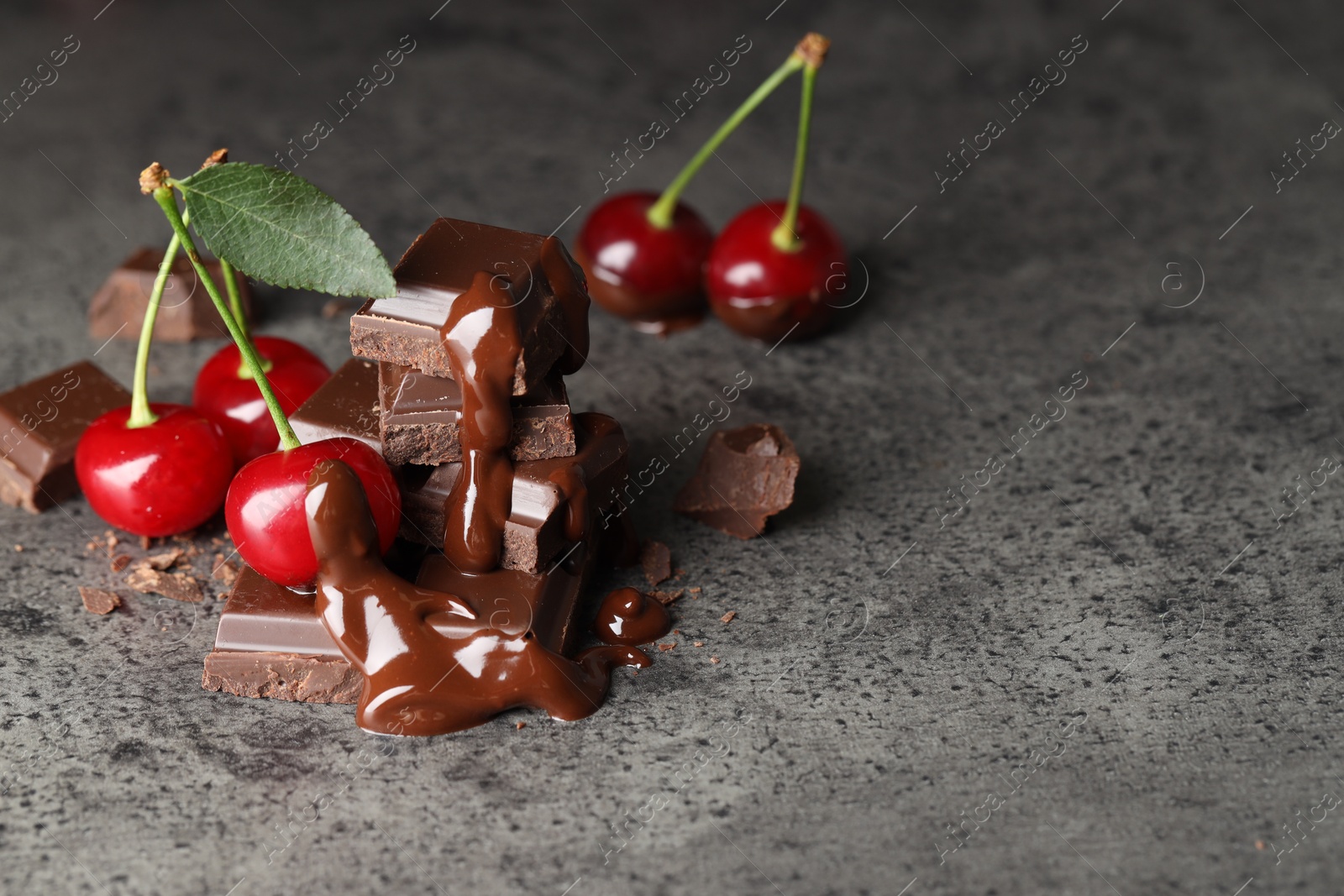 Photo of Fresh cherries with dark chocolate on grey textured table, space for text