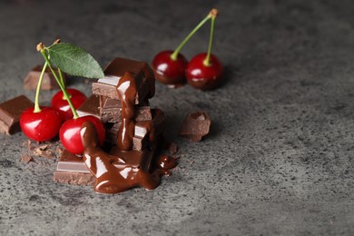 Fresh cherries with dark chocolate on grey textured table, space for text