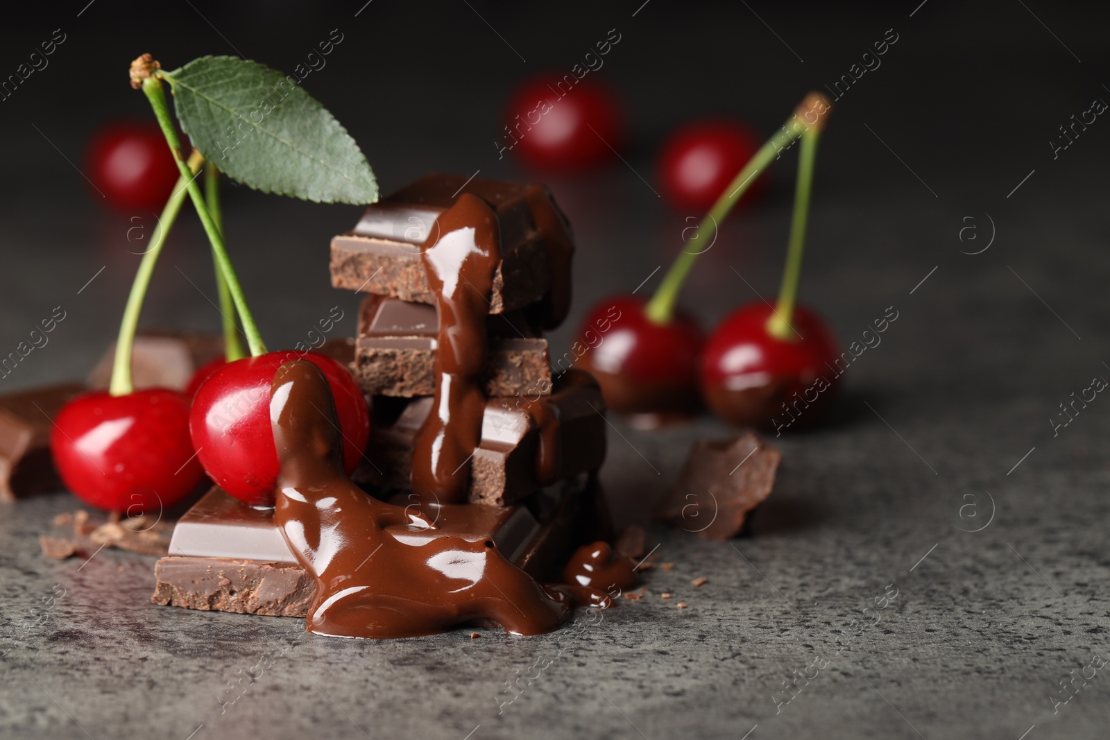 Photo of Fresh cherries with dark chocolate on grey textured table, closeup