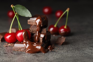 Photo of Fresh cherries with dark chocolate on grey textured table, closeup