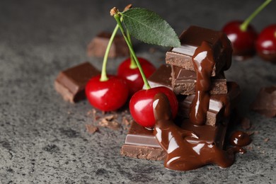 Fresh cherries with dark chocolate on grey textured table, closeup