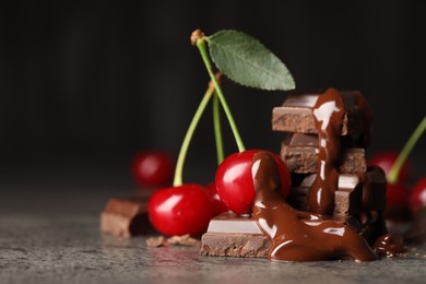 Photo of Fresh cherries with chocolate on grey textured table, closeup