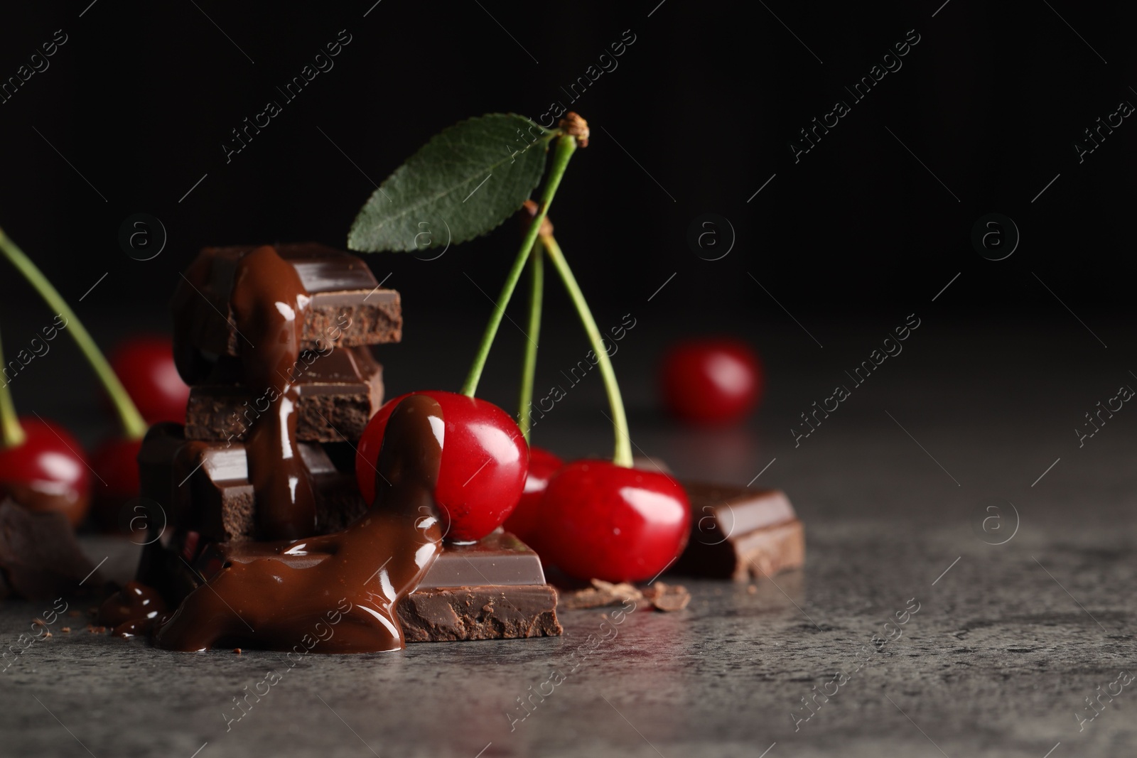 Photo of Fresh cherries with dark chocolate on grey textured table, closeup. Space for text