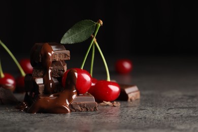 Fresh cherries with dark chocolate on grey textured table, closeup. Space for text