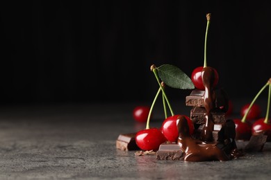 Fresh cherries with dark chocolate on grey textured table, closeup. Space for text