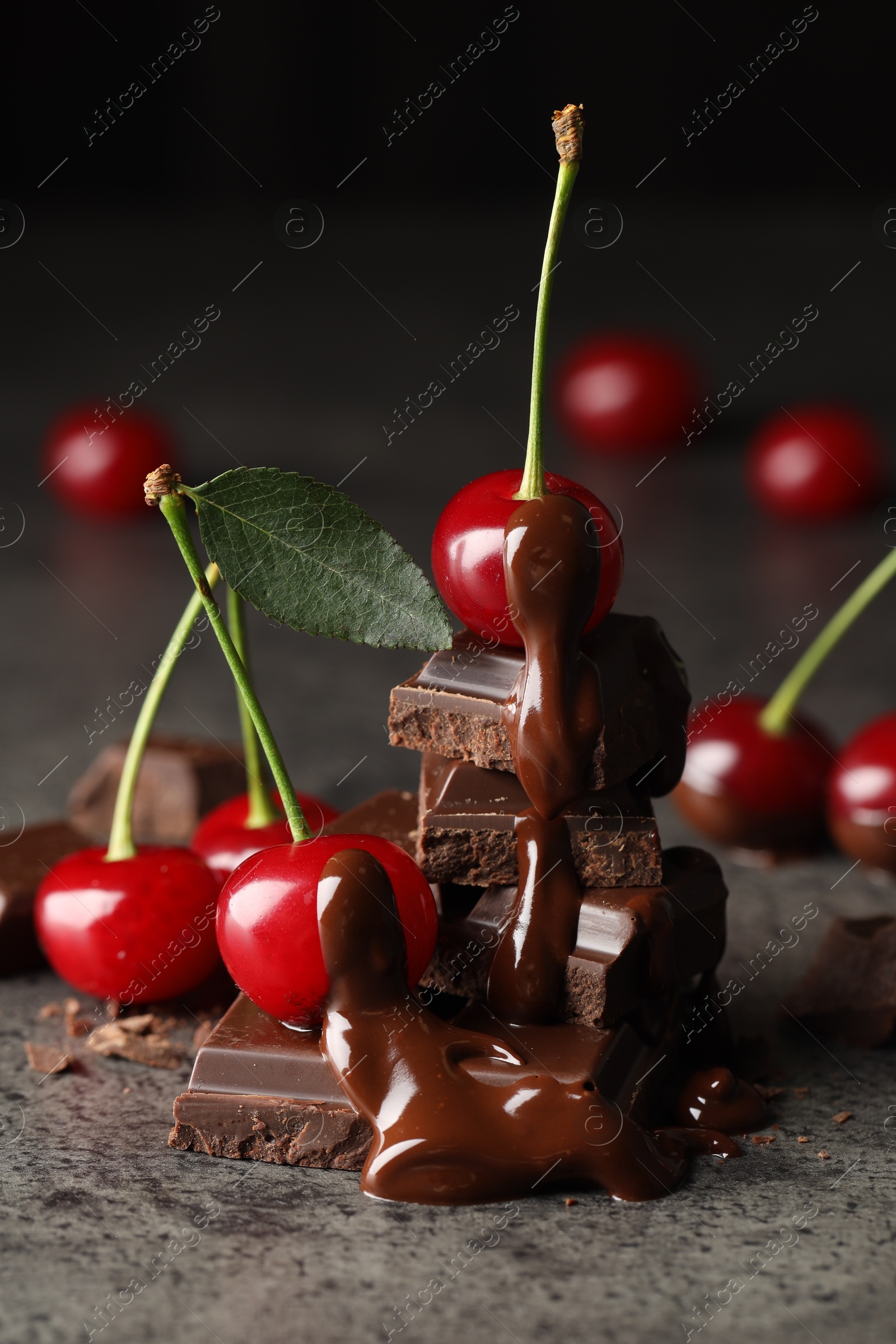 Photo of Fresh cherries with dark chocolate on grey textured table, closeup